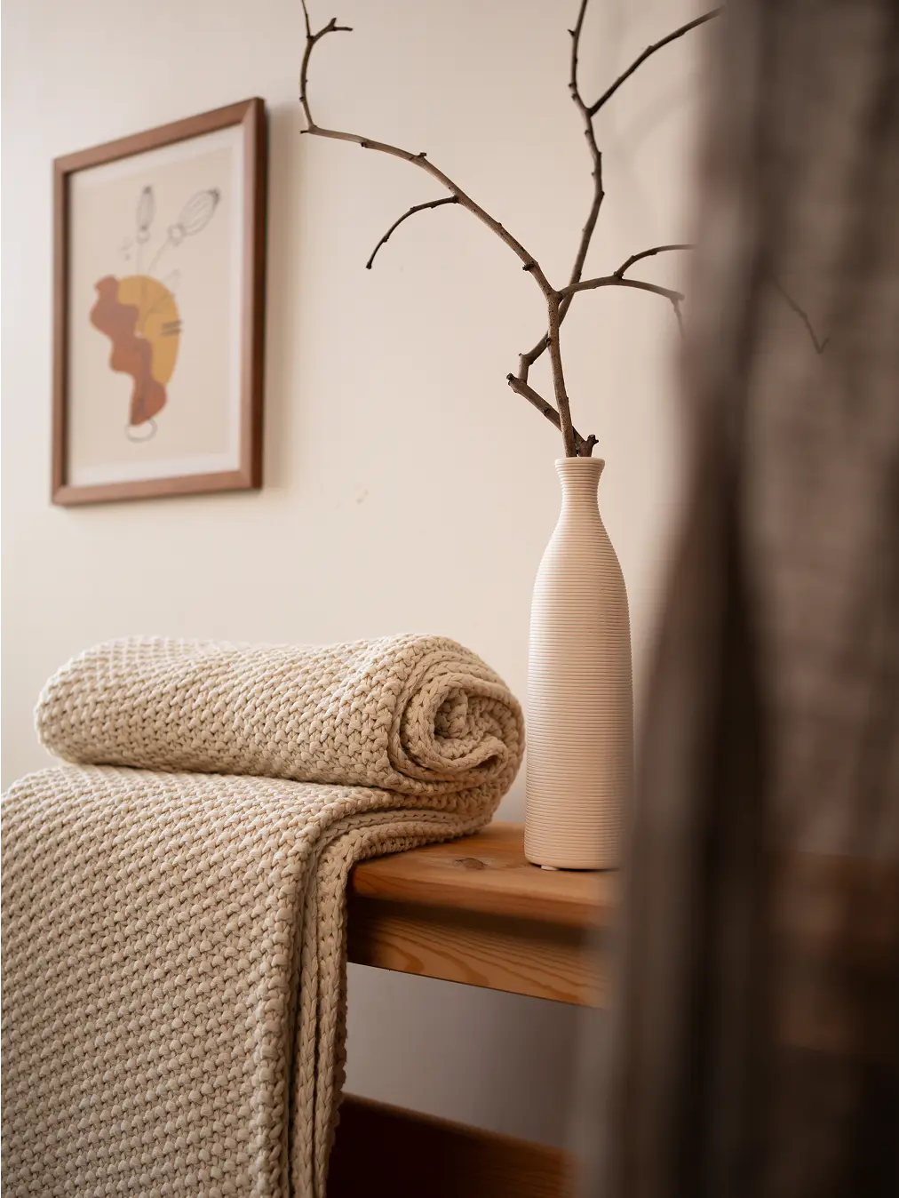Beige Alpine Cotton Knitted Throw neatly rolled on a wooden bench, showcasing its soft, breathable cotton fabric