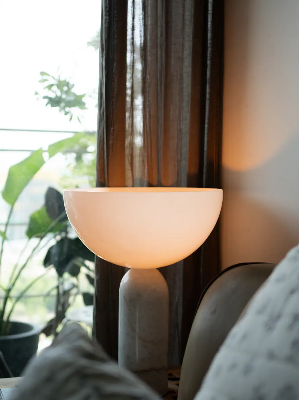 Modern table lamp with white marble base placed by a window with sheer curtains