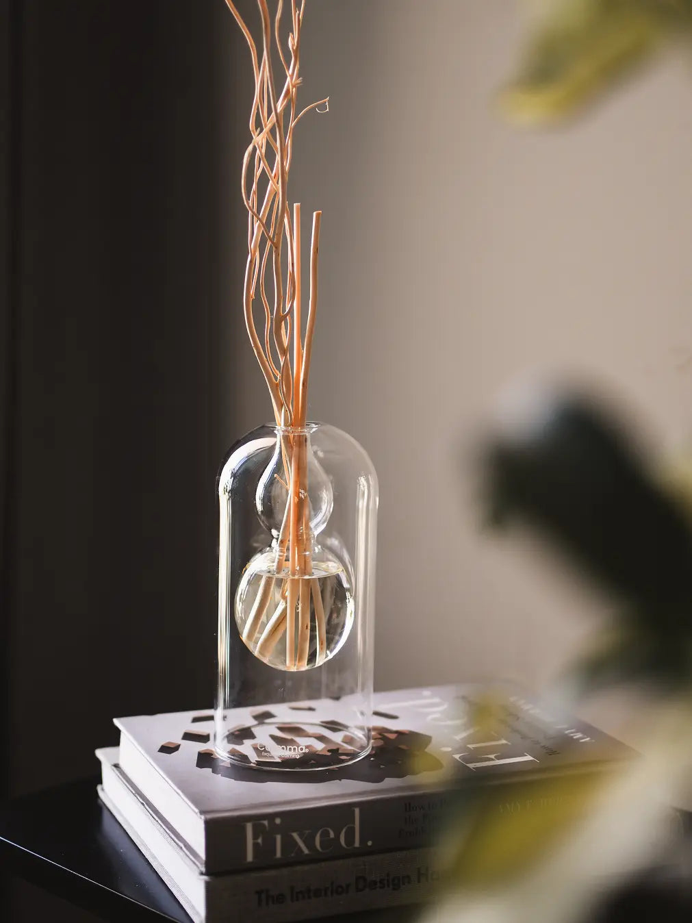 Calmma Glass Reed Diffuser with natural rattan reeds placed on stacked books, diffusing fragrance elegantly.