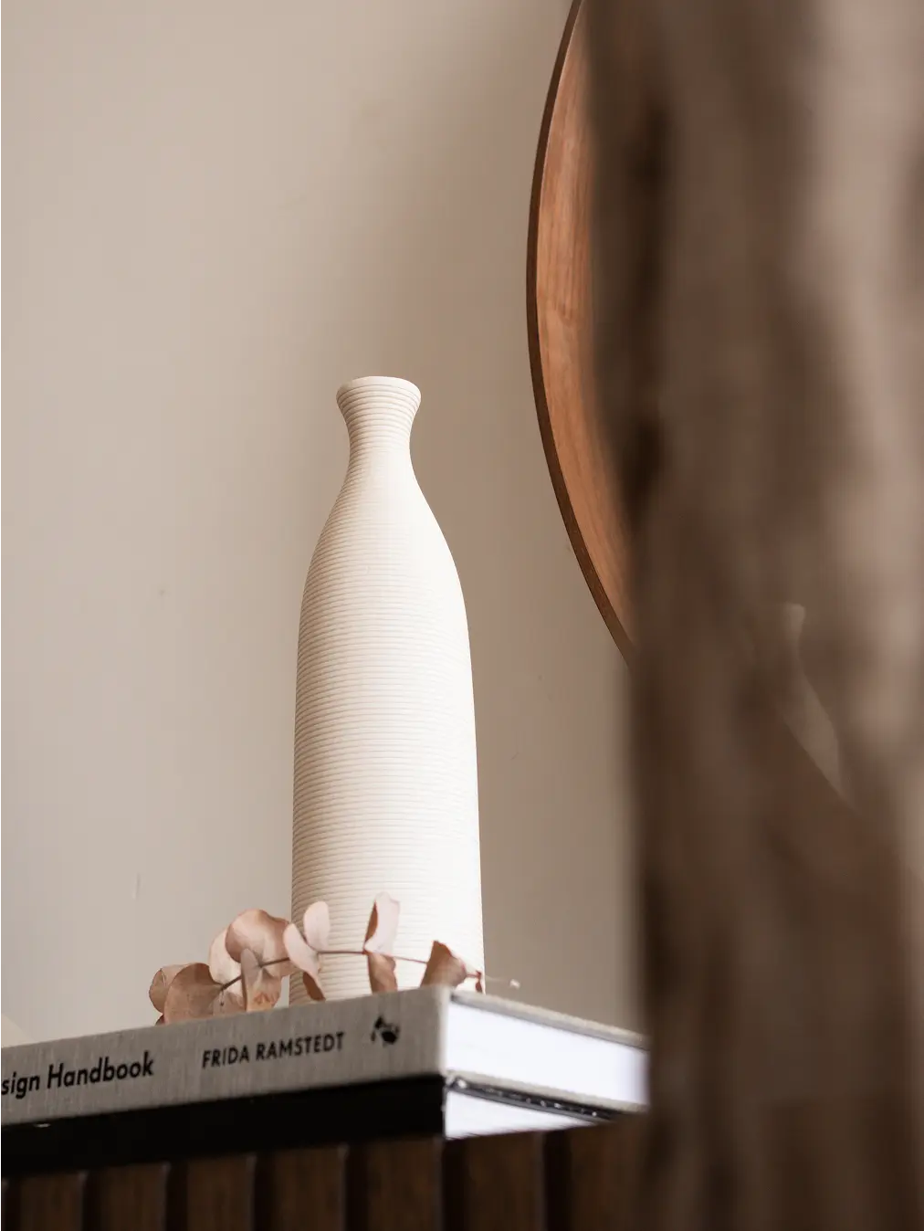 Minimalist Contour Ceramic Vase – White, placed on a wooden shelf with decor books and dried botanicals.