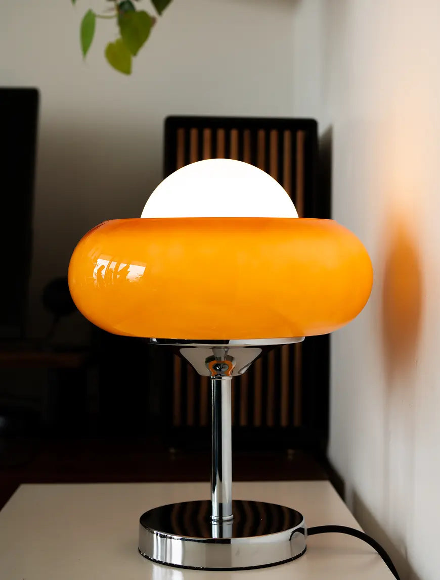 Orange table lamp with a white round shade on a blurred indoor background