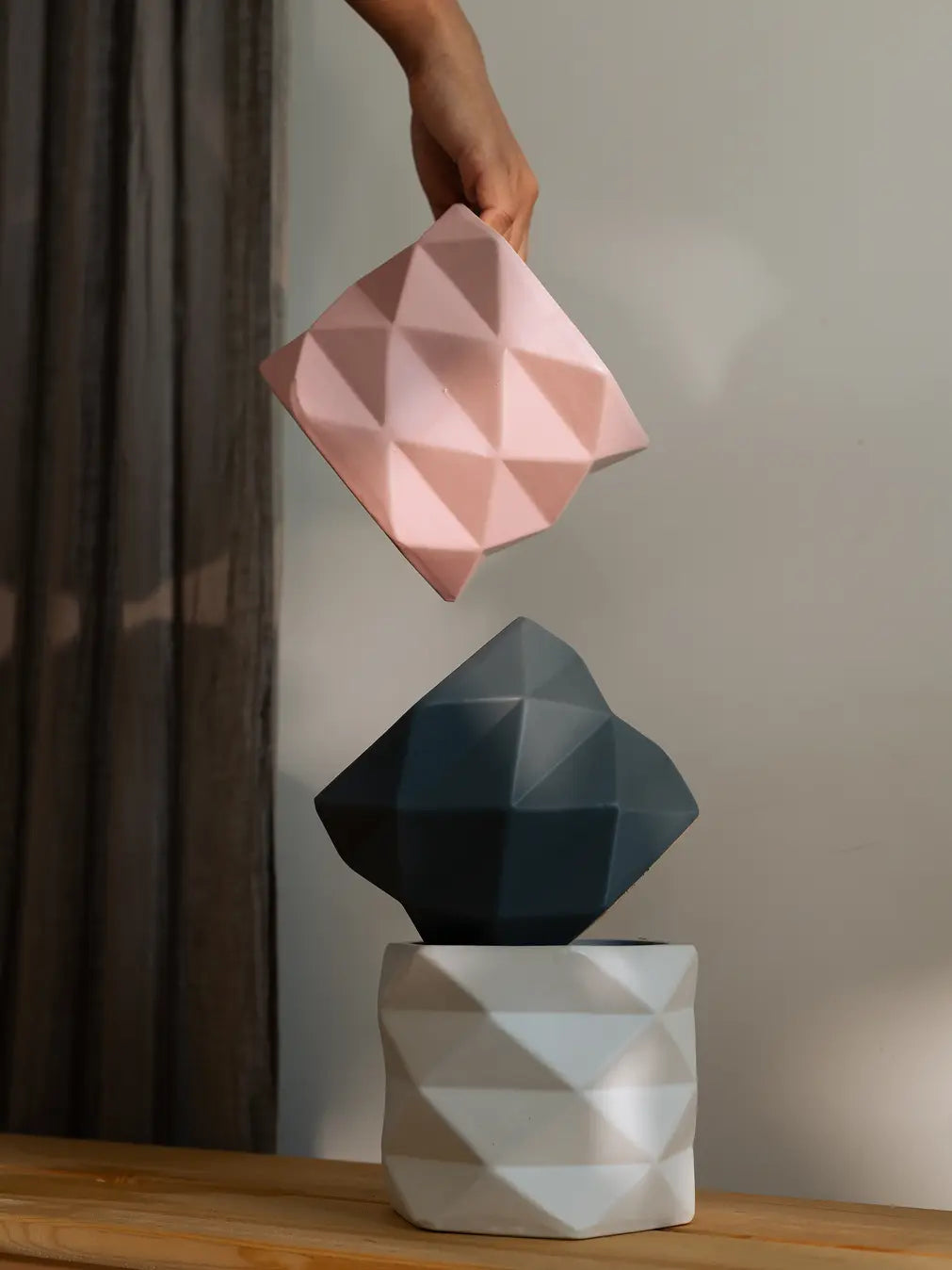 Three Diamond Ceramic Planters in pink, grey, and white, being arranged stylishly.