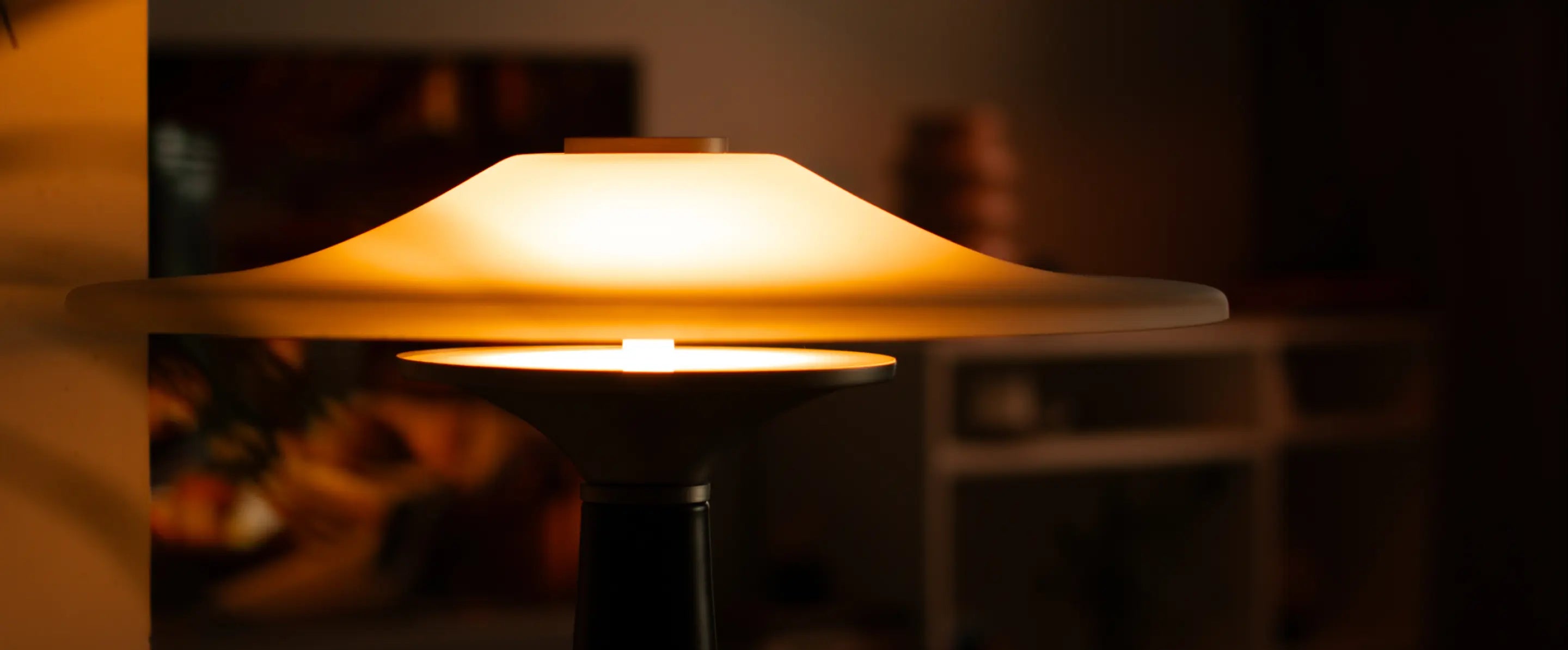 Side view of illuminated Disc Glass Table Lamp showing layered frosted glass and warm glow
