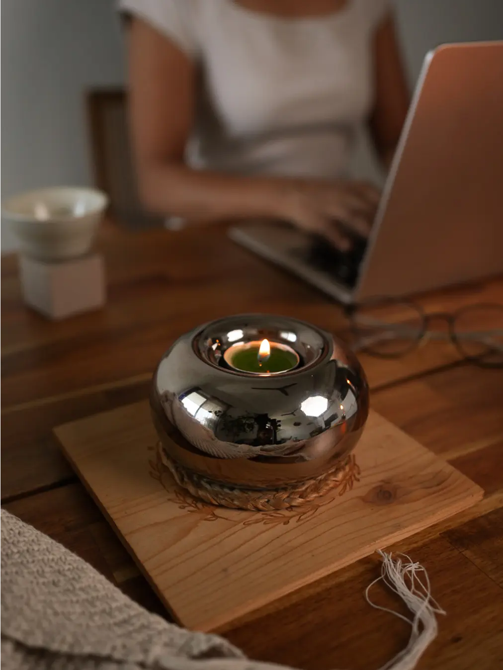 Donut Chrome Candle Holder with a lit tealight candle, creating a cozy ambiance on a wooden table.