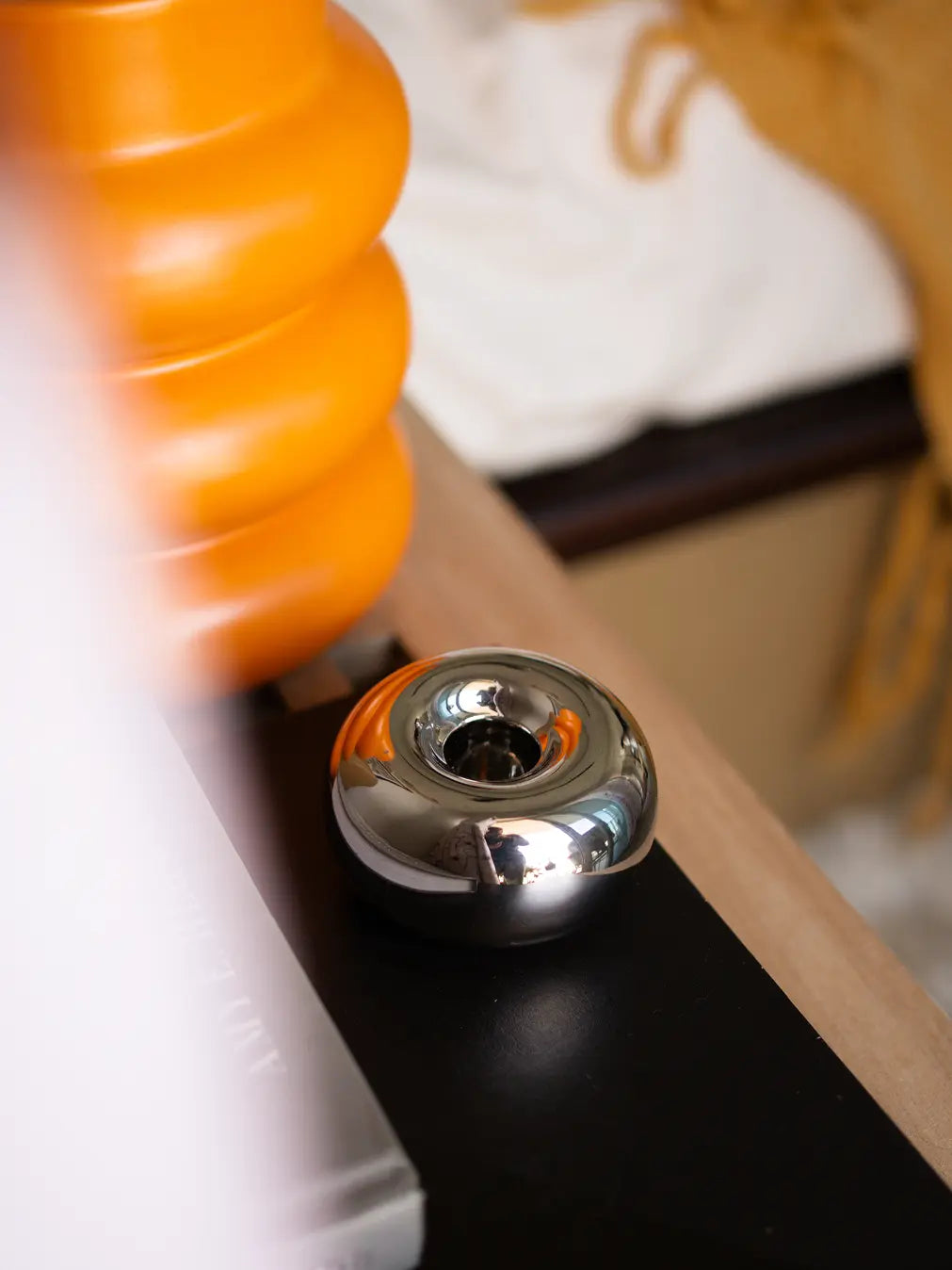 Modern Donut Chrome Candle Holder on a black bedside table, reflecting vibrant orange decor accents.