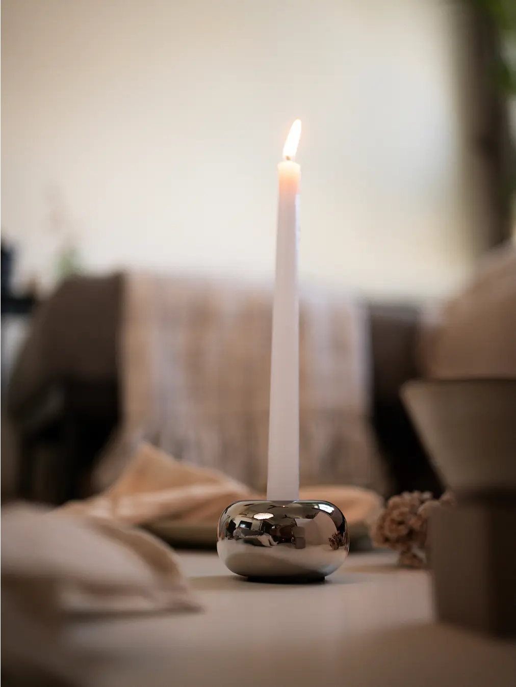 Donut Chrome Candle Holder holding a tall white taper candle, styled in a minimalist dining setting.