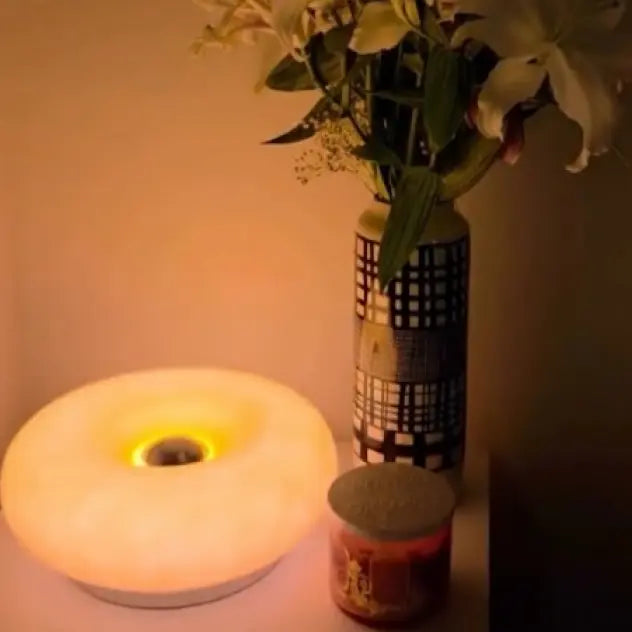 Decorative donut lamp, vase with flowers, and small candle on a surface with warm lighting.