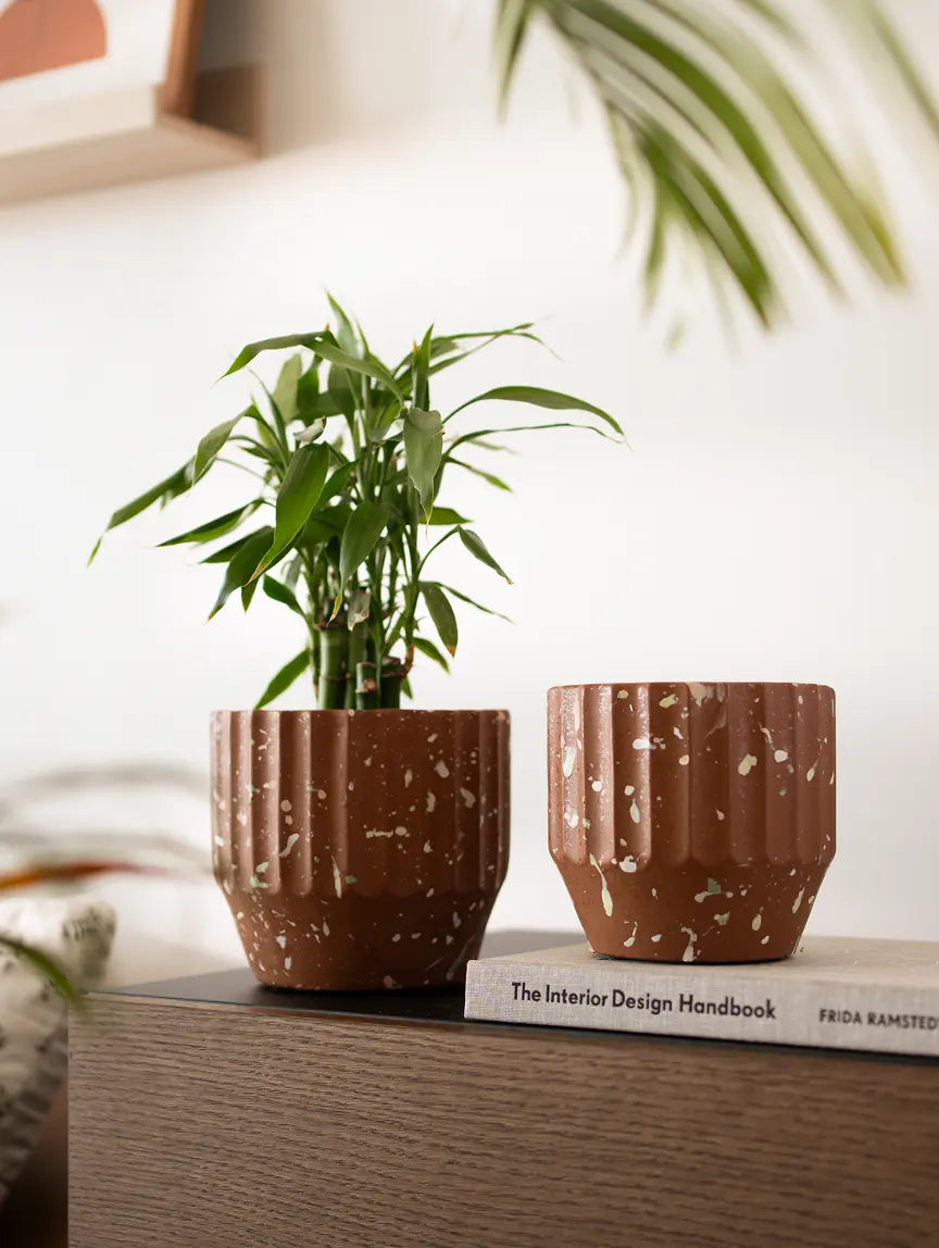 A pair of Marvellous Concrete Planters - Brown in different sizes, styled on a wooden cabinet with an interior decor book.