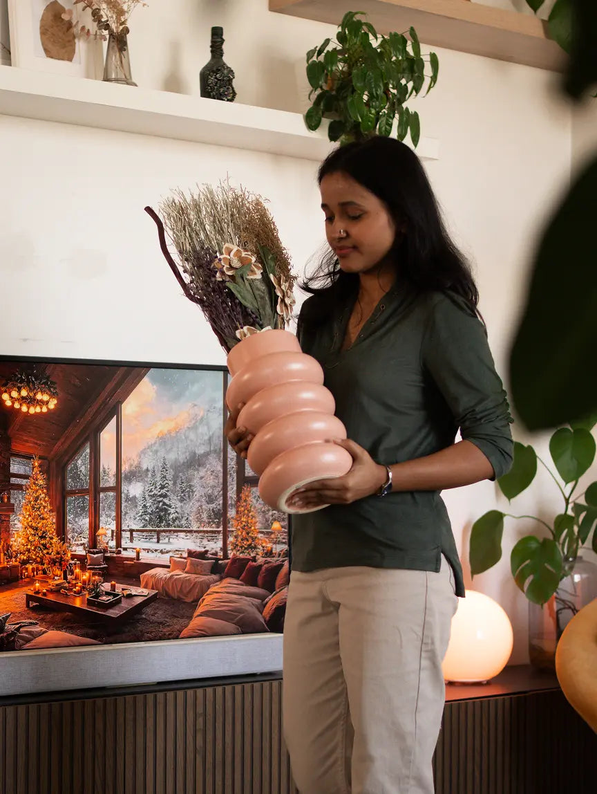 Woman holding the Orbit Ceramic Vase - Peach, featuring a sculptural design and dried floral arrangement, in a cozy living space.