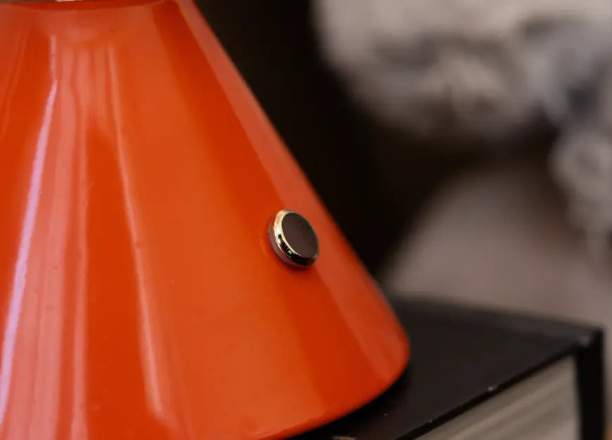 Close-up of the Dusk Table Lamp’s orange base with a sleek metallic power button
