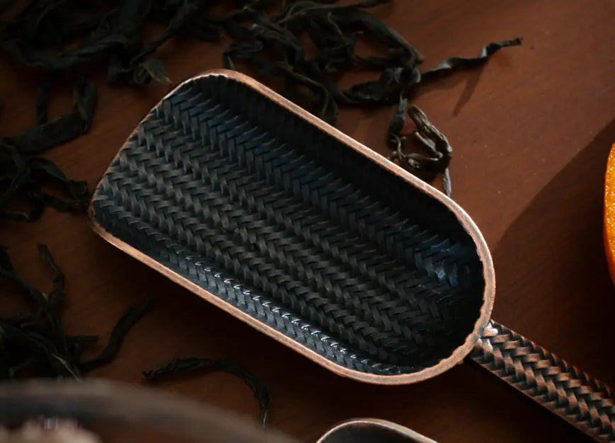 Intricately woven Vintage Spoon with a dark metallic finish, resting among tea leaves.
