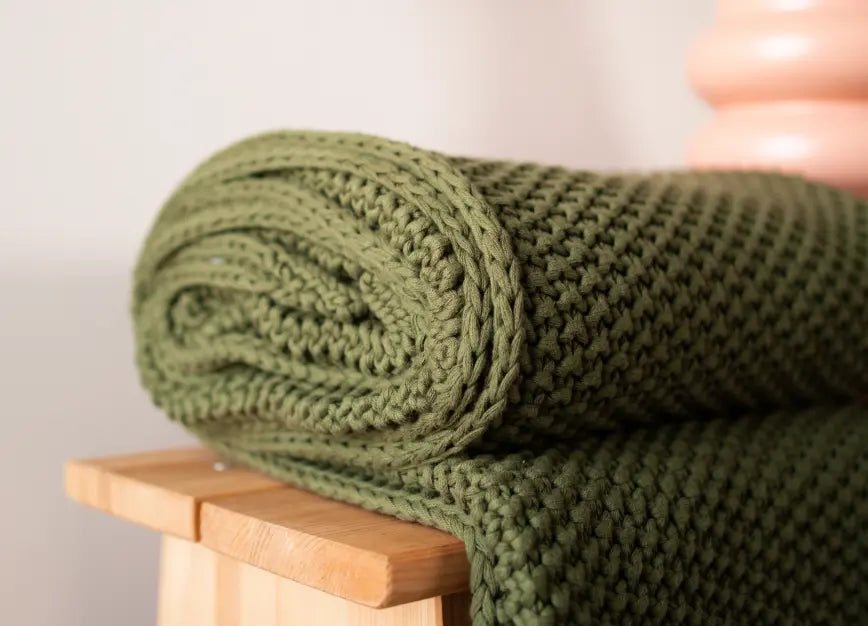 Green Alpine Cotton Knitted Throw on a bench, showcasing its thick, breathable cotton fabric.