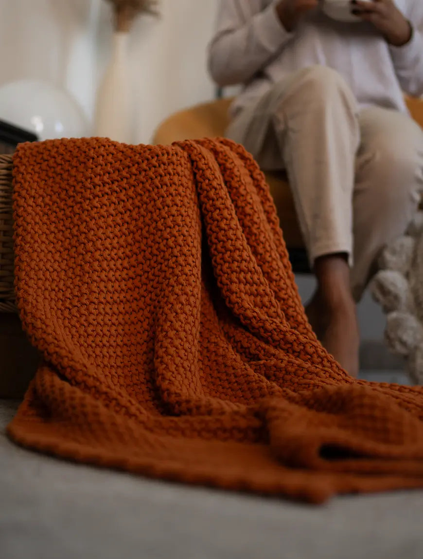 Mustard Alpine Cotton Knitted Throw draped over a basket, styled beside a warm-toned interior setting.