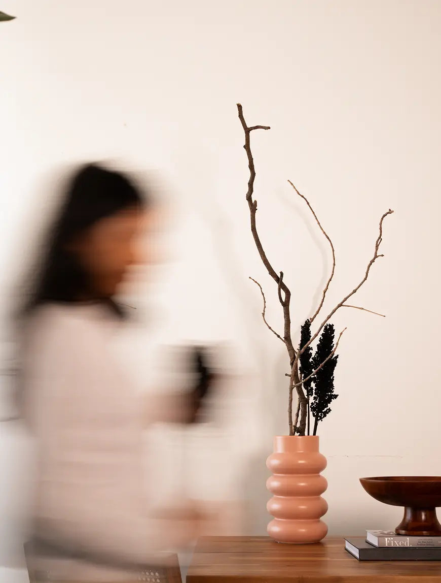 Woman placing tall branches into the Orbit Ceramic Vase - Peach, styled as a centerpiece.