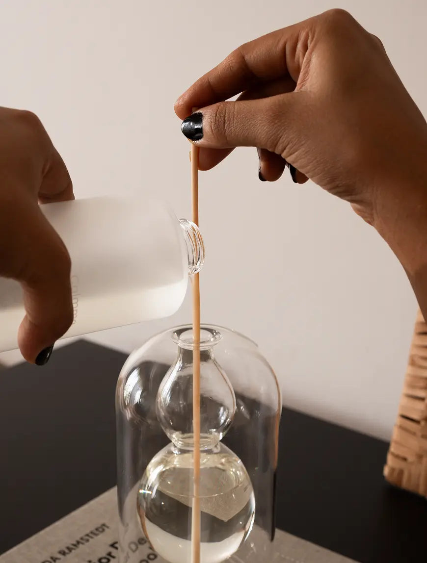 Pouring fragrance oil into the Calmma Glass Reed Diffuser's inner glass chamber, highlighting its precise design.
