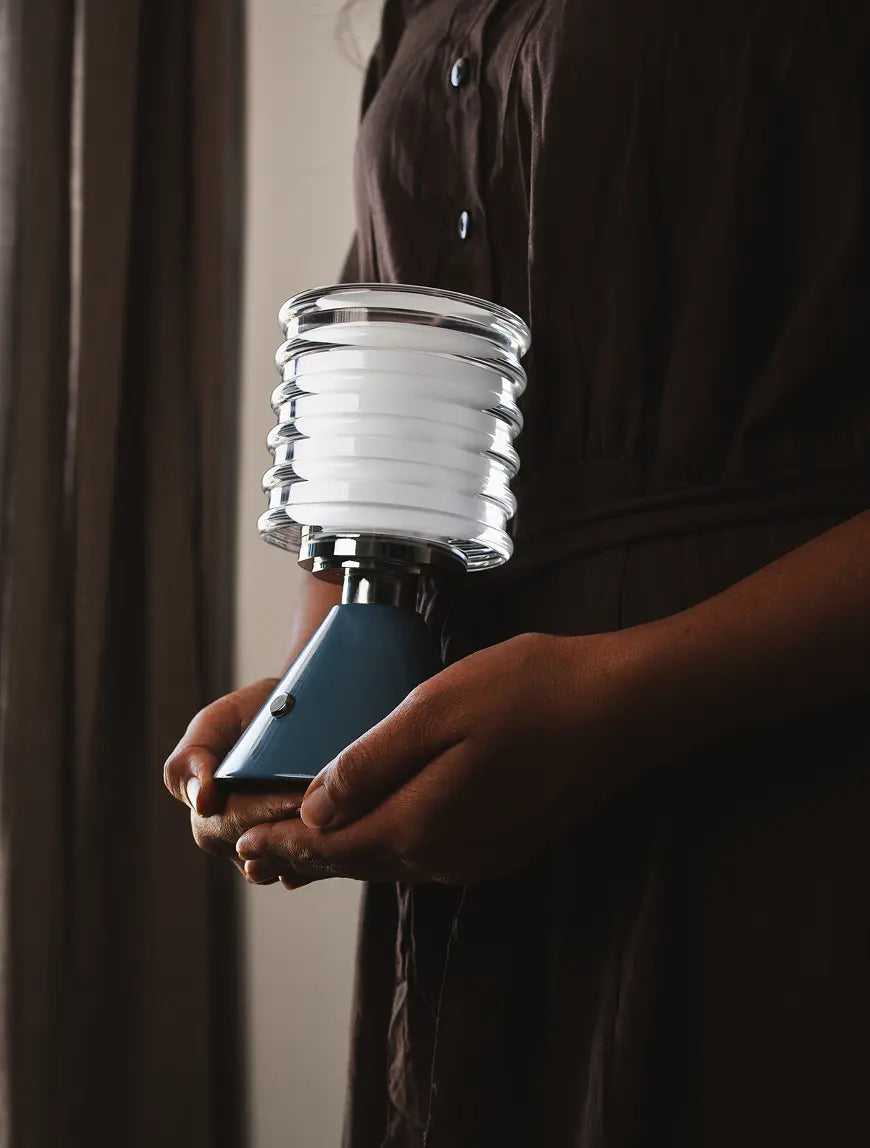 Dusk Table Lamp with a sleek aluminum base and rechargeable LED, held in hand for portability.