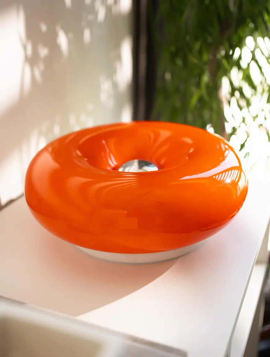 Close-up of Donut Glass Lamp's sleek chrome touch control on its vibrant orange glass body.