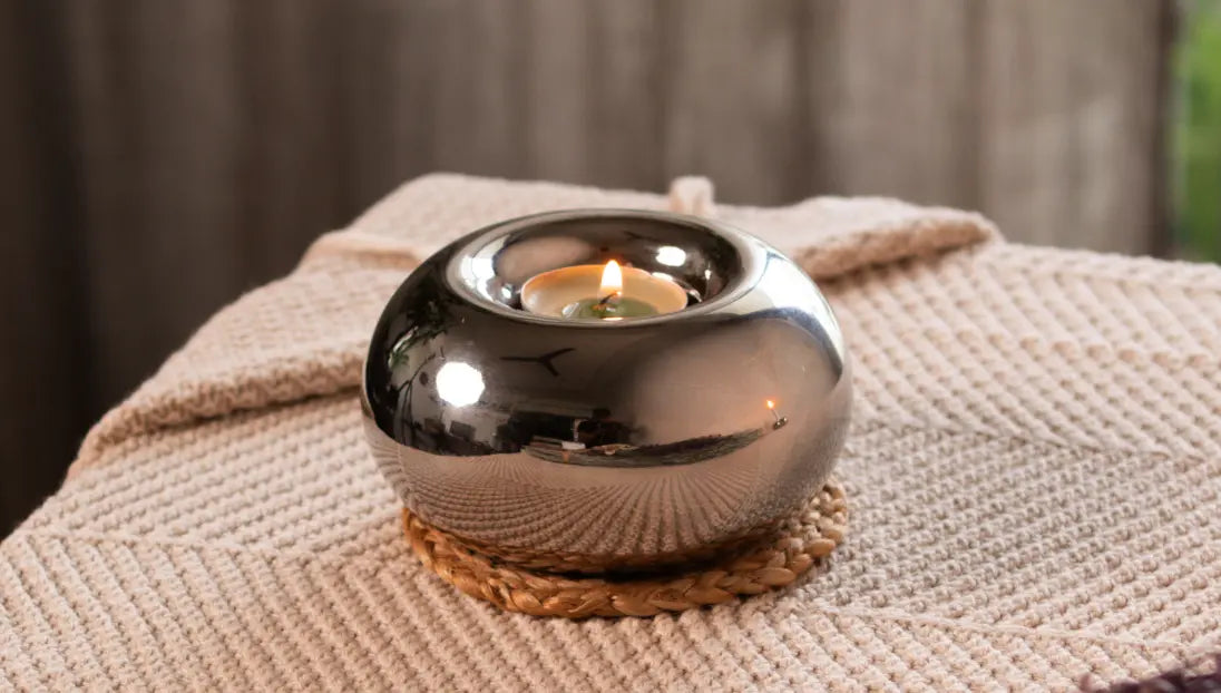 Donut Chrome Candle Holder with a lit tealight, placed on a woven coaster for a warm ambiance.
