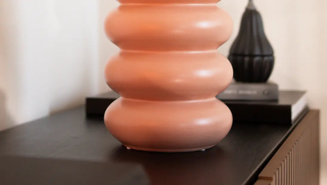 Orbit Ceramic Vase - Peach on a wooden shelf, next to a black decorative accent for contrast.