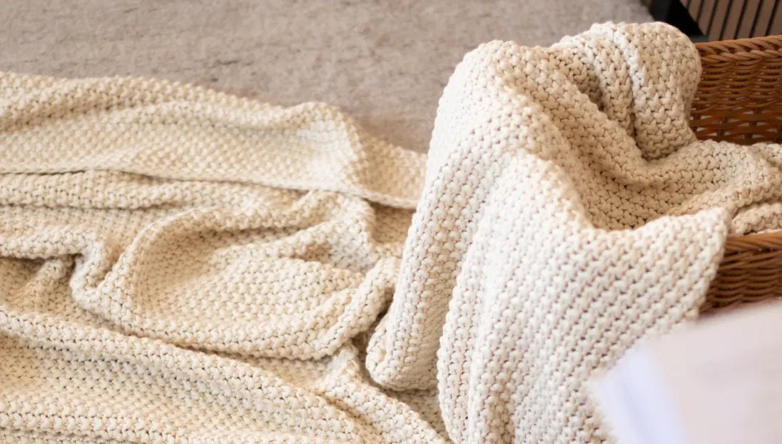 Off-white Alpine Cotton Knitted Throw loosely spread in a basket, emphasizing its airy, handwoven texture.