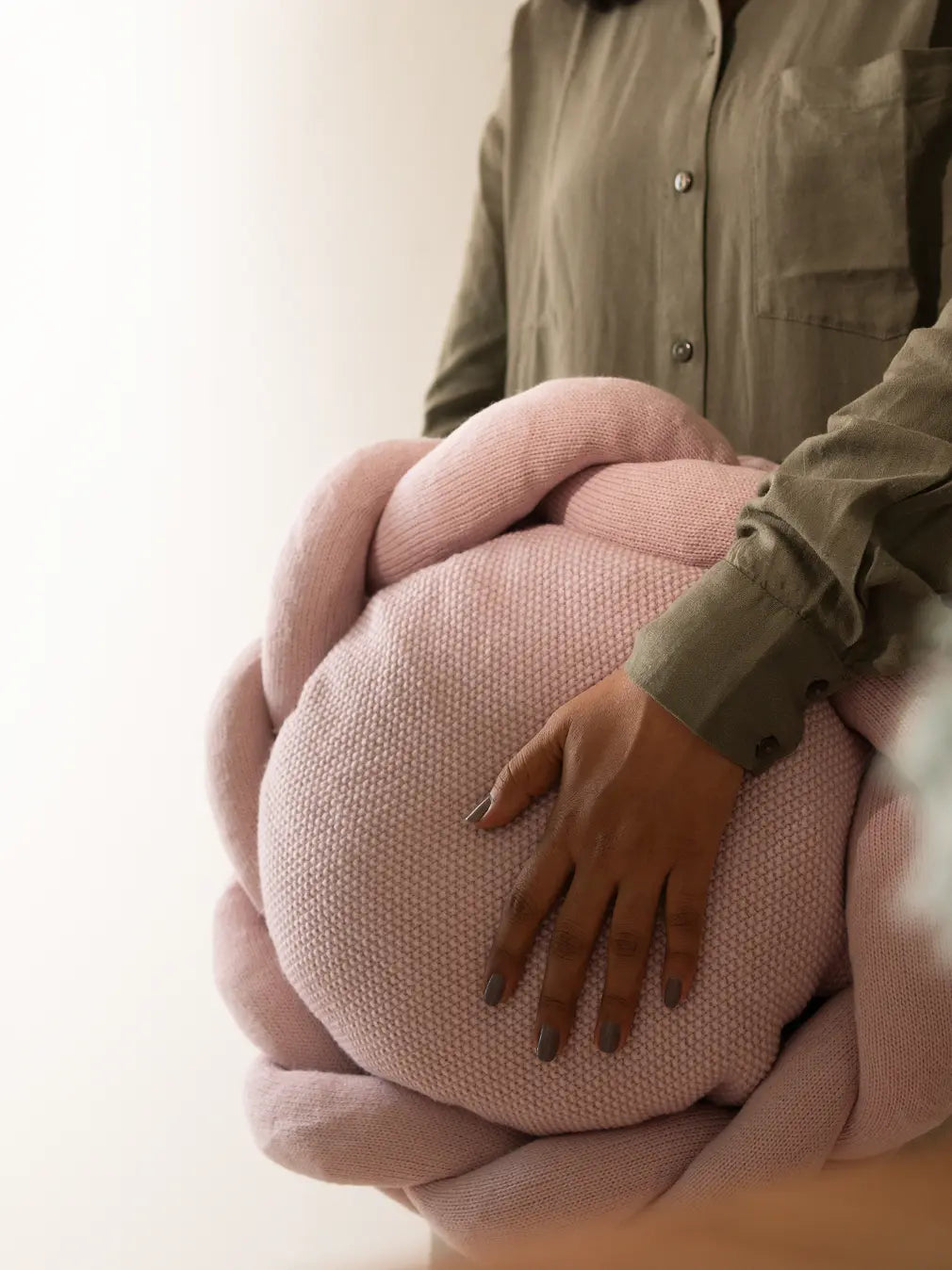 Halo Nest Cushion in blush pink, highlighting its soft knitted fabric and braided edges.
