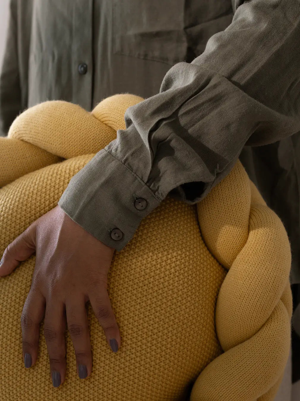 Hand resting on yellow Halo Nest Cushion with braided knit ring and textured wool surface