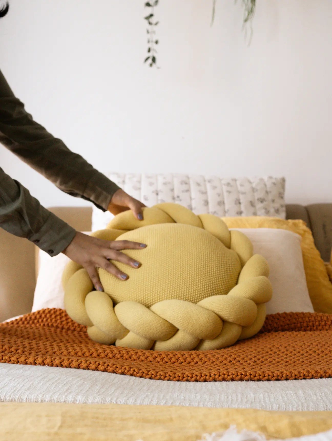 Hands styling Halo Nest Cushion on a beige bed with cozy throw