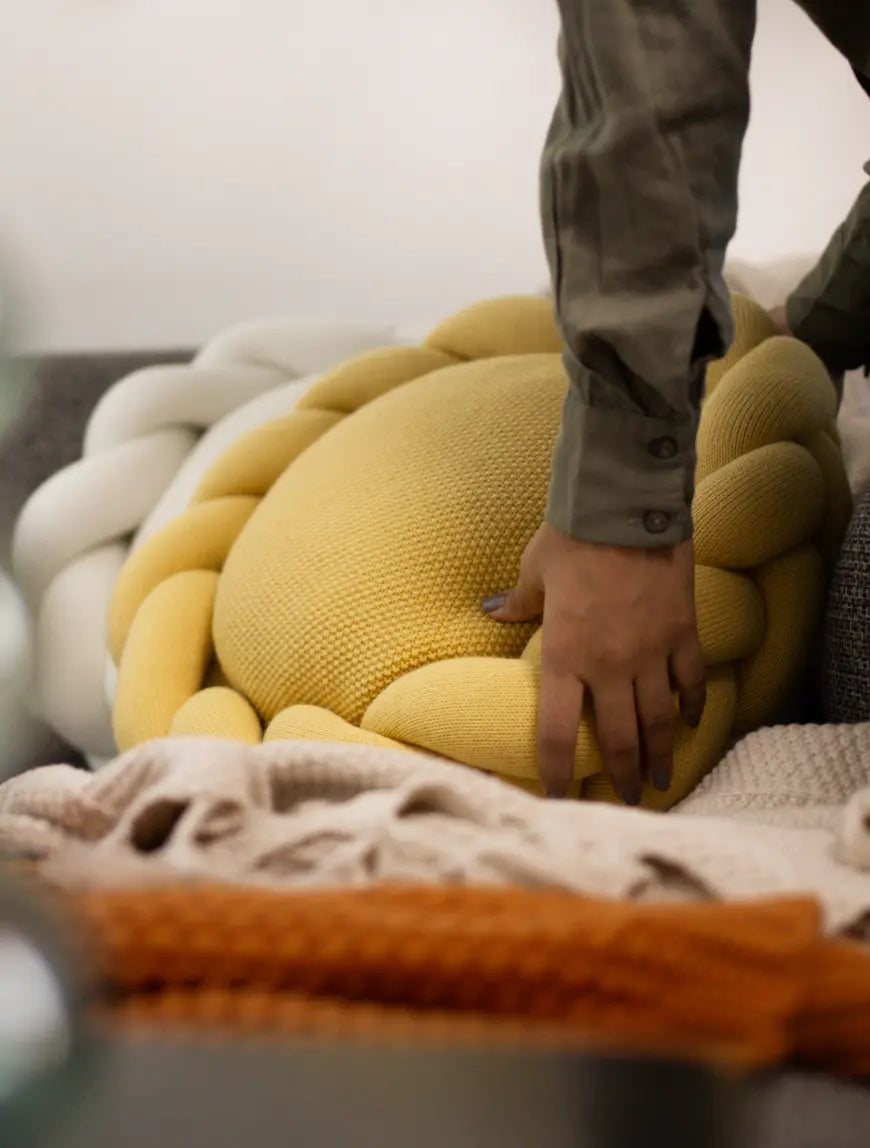 Halo Nest Cushion placed on a grey sofa with layered cozy throws