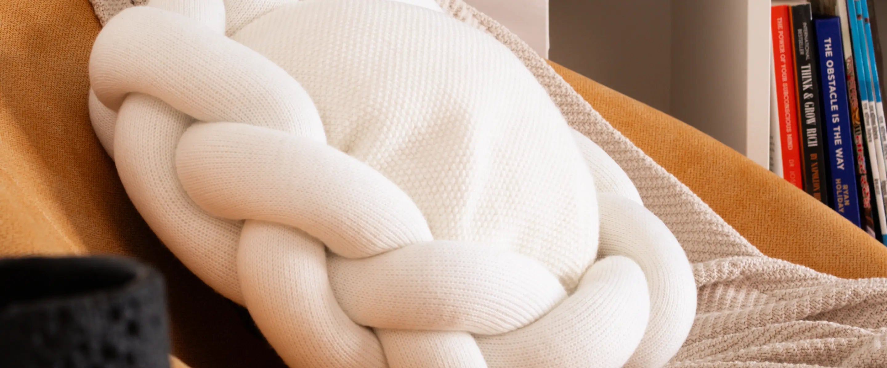 White round braided cushion styled on chair with books in a cozy reading nook