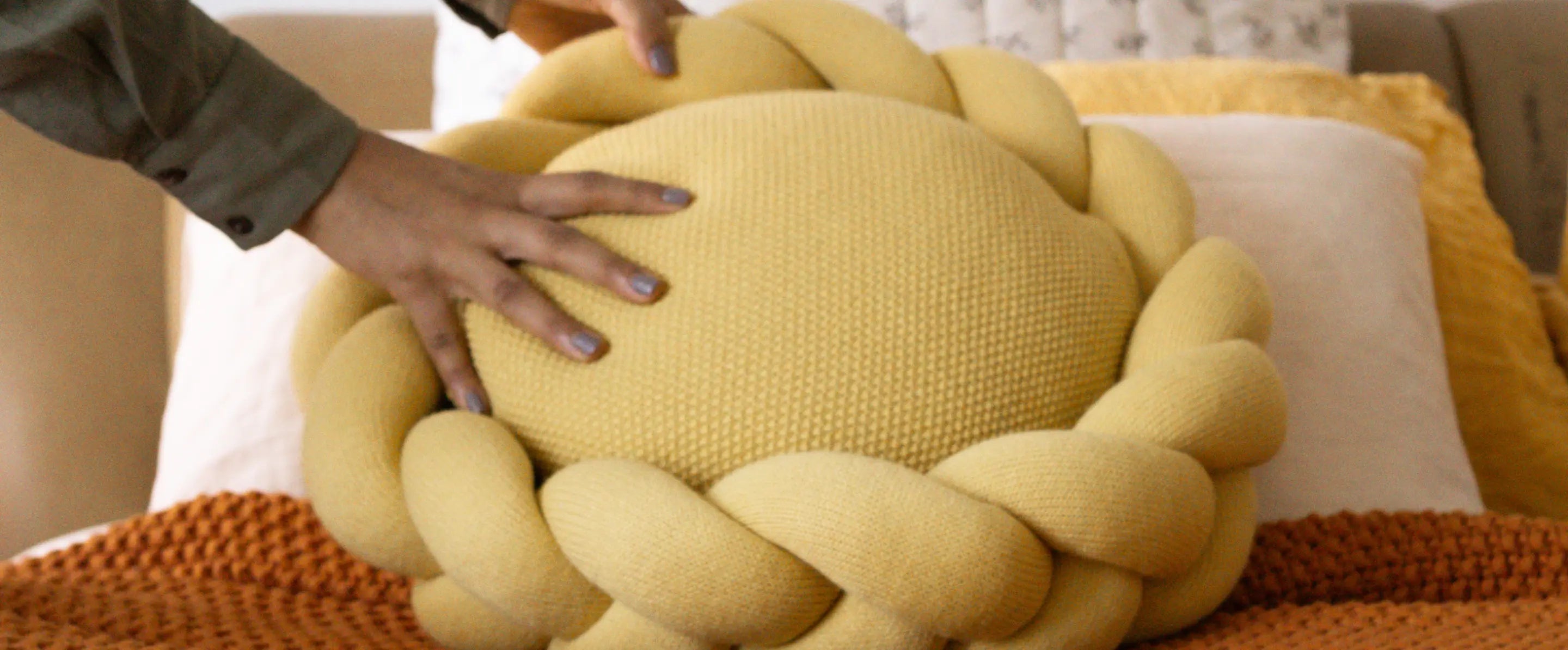 Gharko Yellow round cushion with braided knit ring styled on bed with orange throw