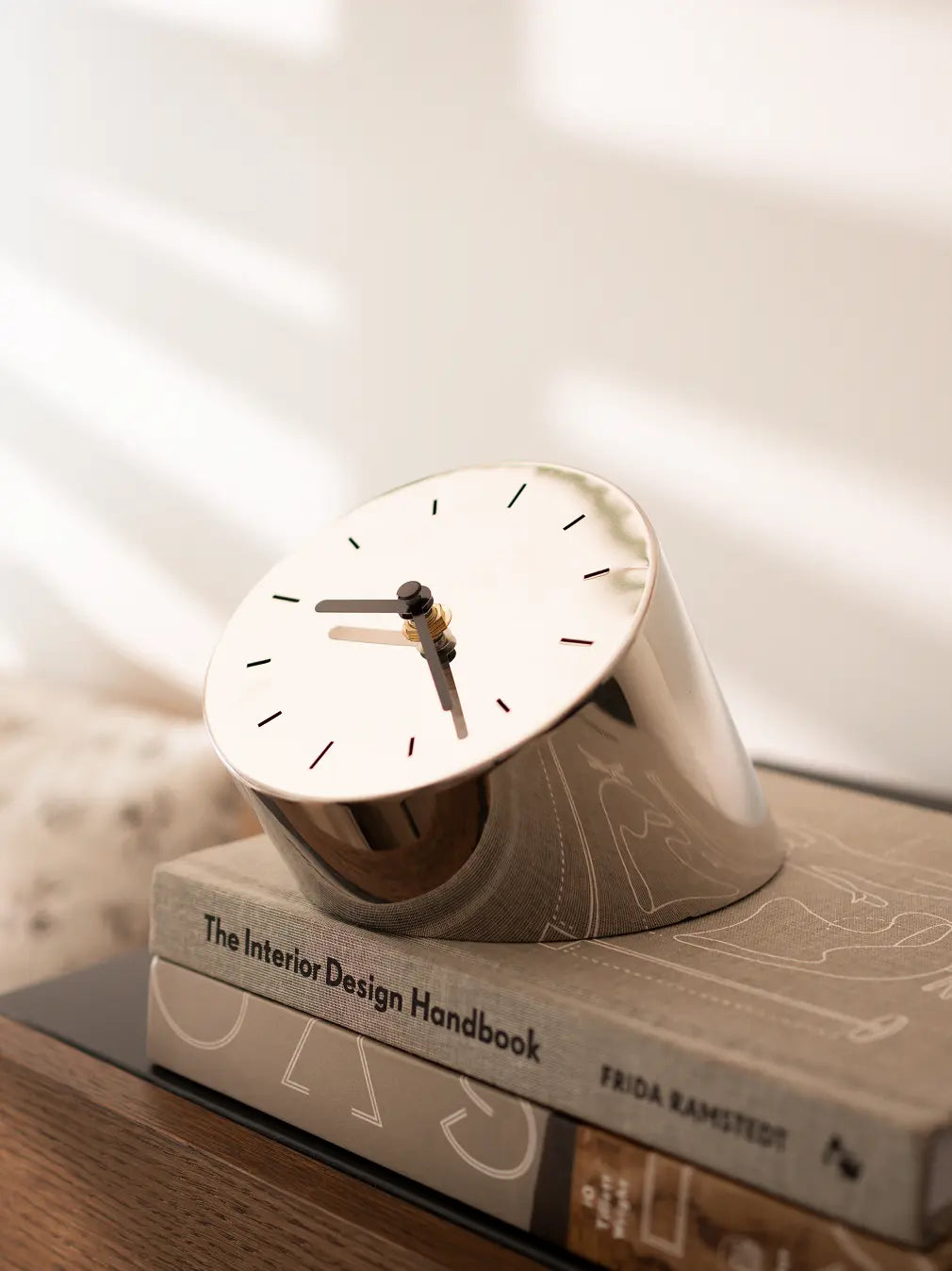 Silver metal table clock with black dial styled on books in soft morning light