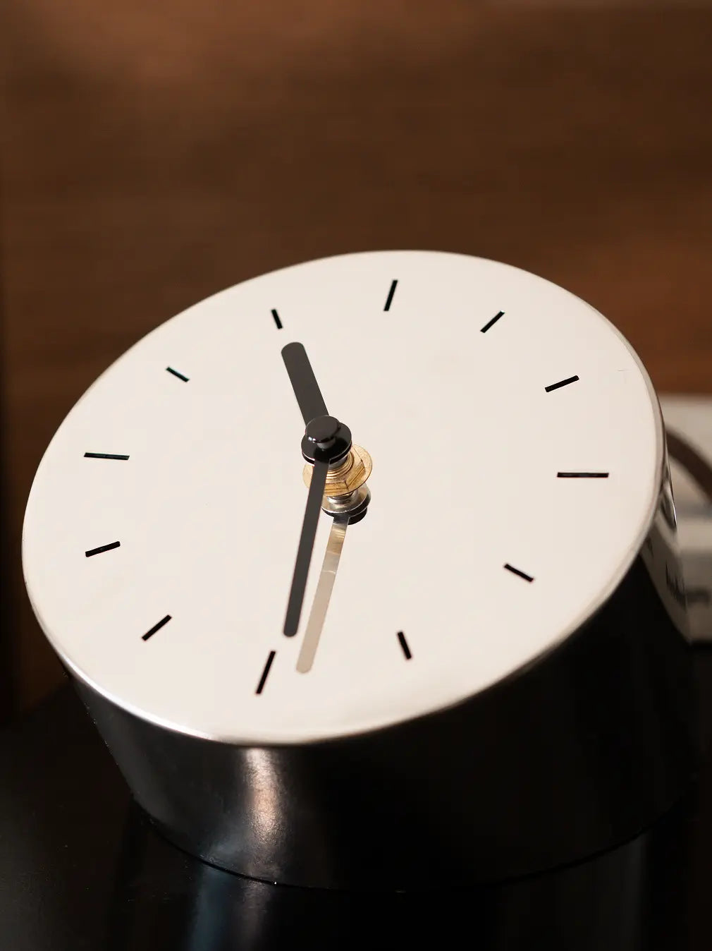 Minimal table clock with black hands and reflective face shown in close-up view