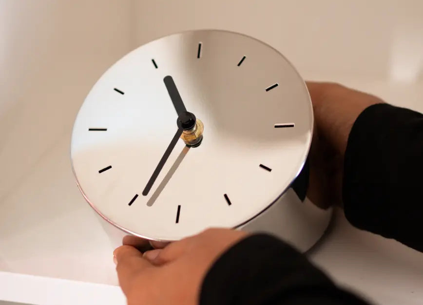 Hands placing Horizon Metal Table Clock on white shelf with minimalist modern styling