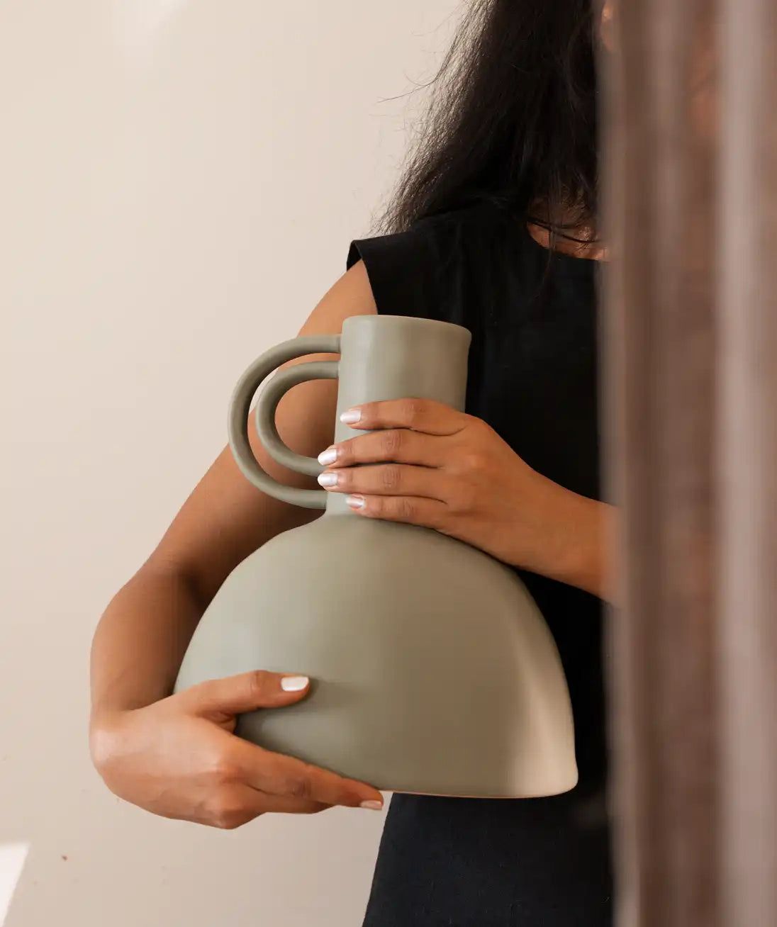 Person holding a light gray vase with two handles against a neutral background