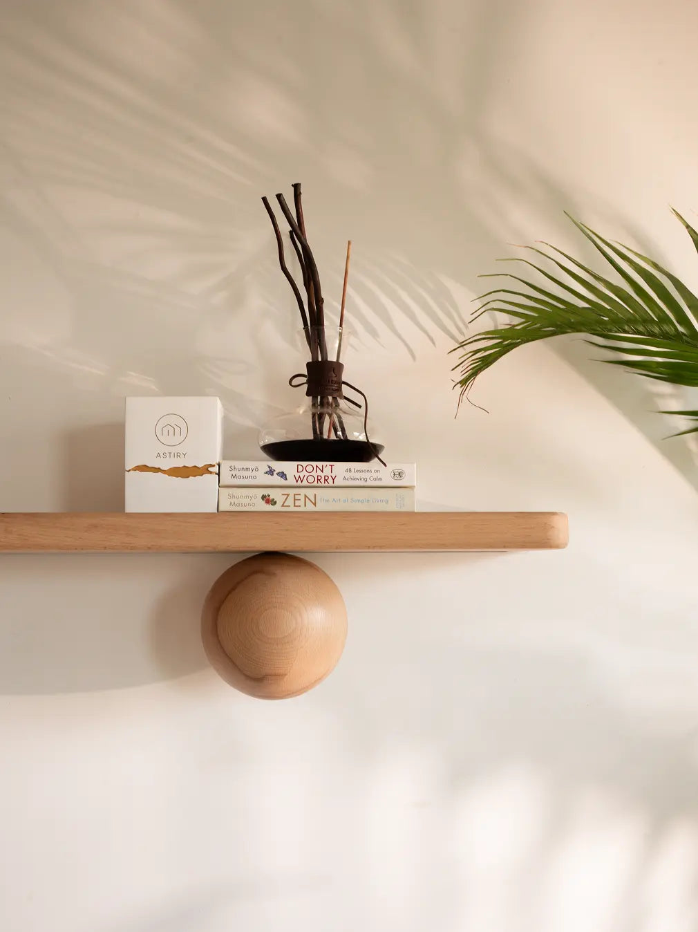 Wooden floating shelf with a vase, books, and a ball on a light background