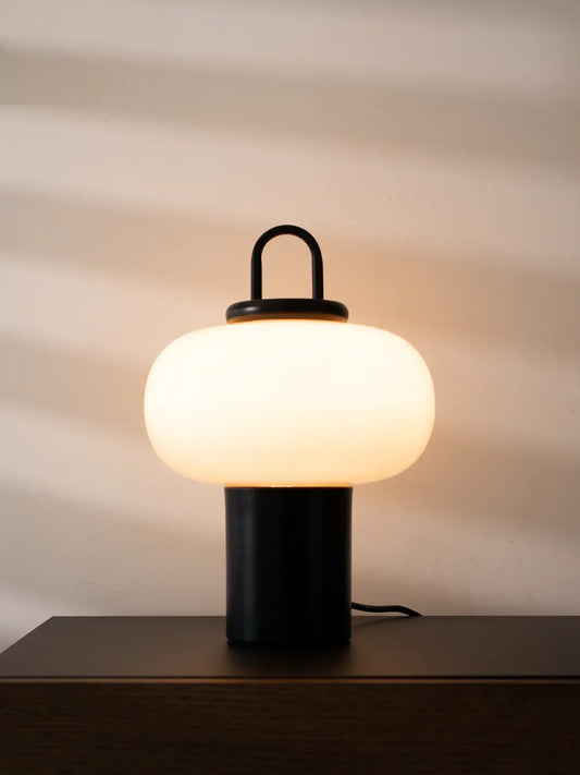 Lysa Glass Table Lamp with black metal base and warm white glow on a dark console table