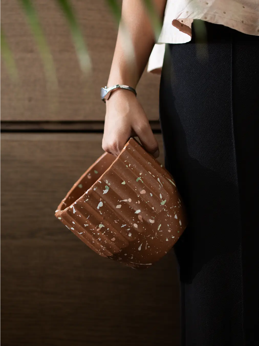 Hand holding the Marvellous Concrete Planter - Brown, showcasing its terrazzo speckled finish and fluted texture.