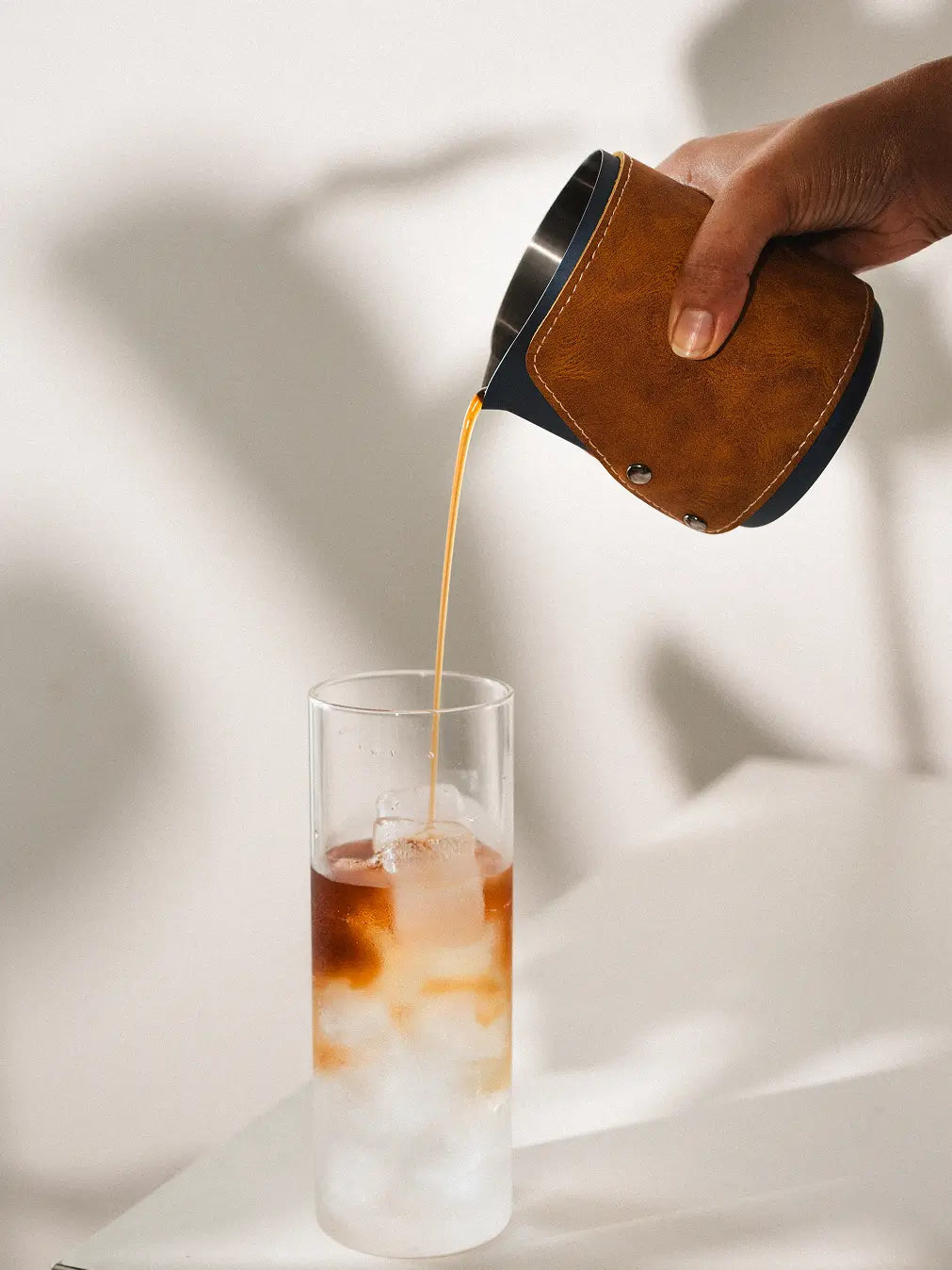 Hand pouring black coffee from the Brista Milk Pitcher with a leather grip and ergonomic handle.
