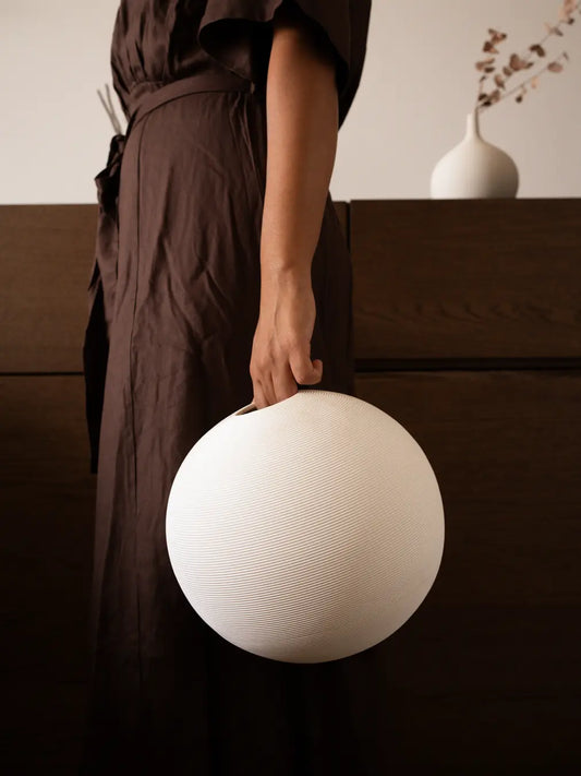 Moon Ceramic Vase in white, elegantly held by hand, showcasing its round sculptural form.