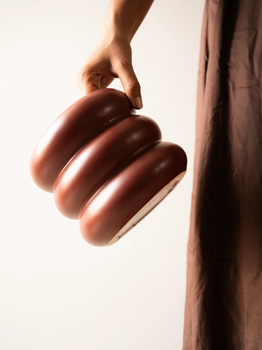 Hand holding the Orbit Ceramic Planter - Maroon, showcasing its smooth design.