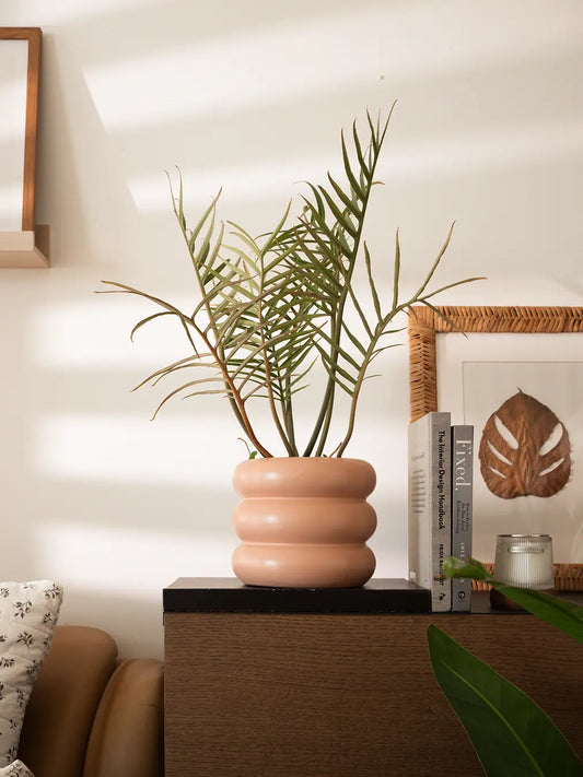 Orbit Ceramic Planter - Peach with a tall plant, placed on a wooden console in soft natural light.