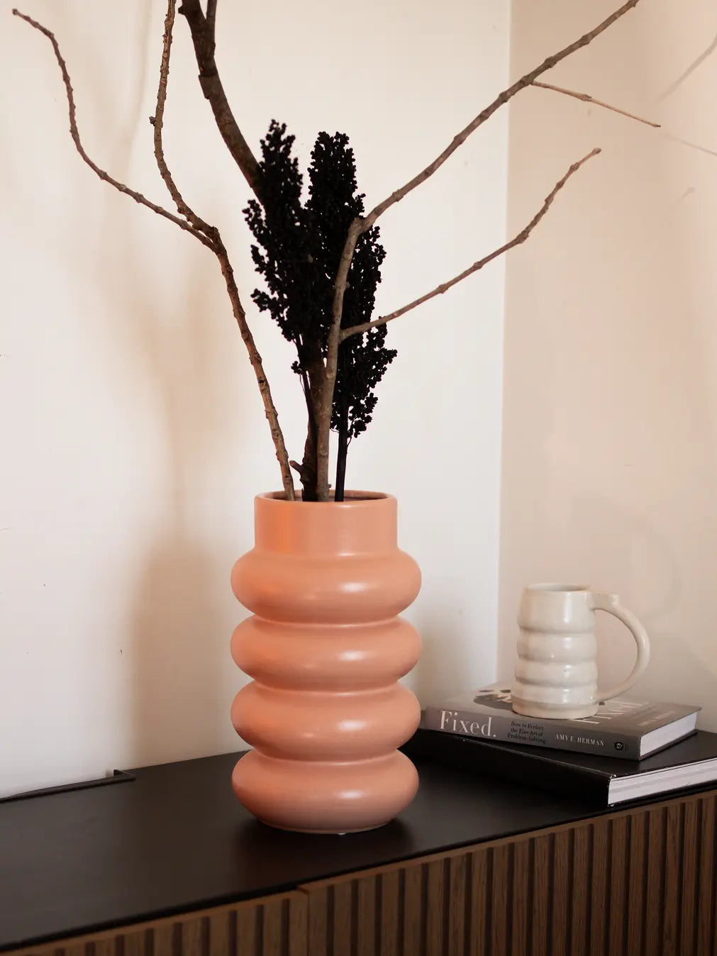 Orbit Ceramic Vase - Peach, featuring a sculptural ripple design, placed on a black console table.