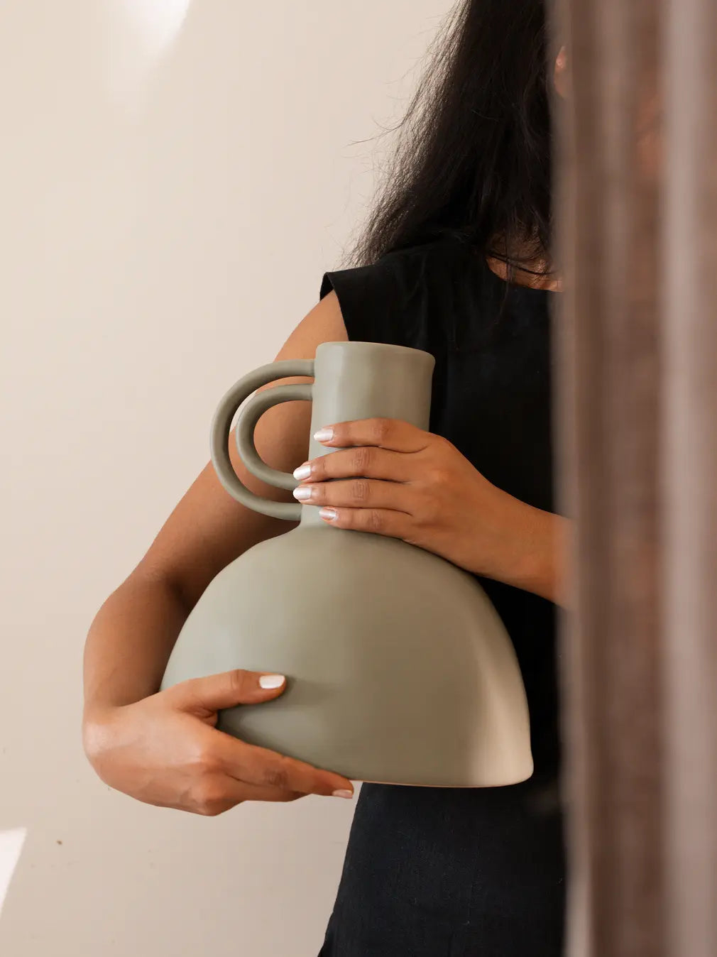 Person holding a green ceramic vase with a neutral background