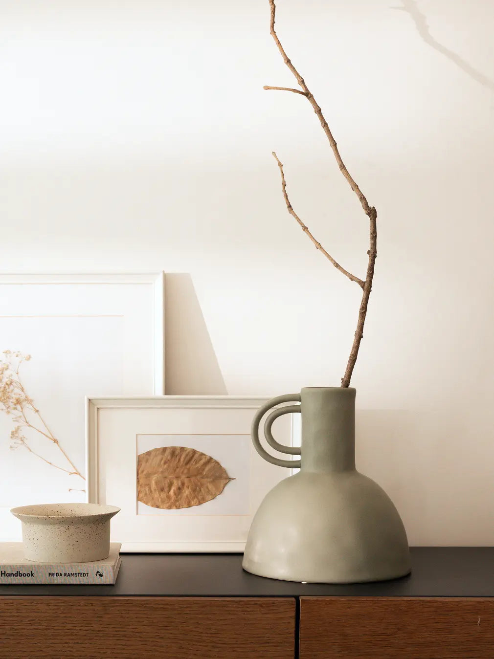 Green ceramic flower vase with decorative items, including a framed artwork and Kokedama pot on a wooden surface.