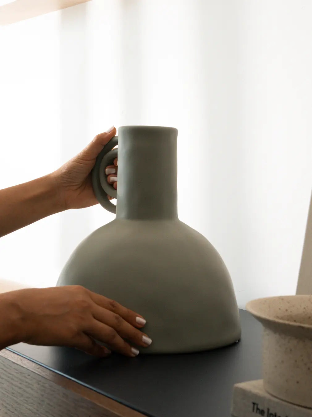 Person holding a Japandi vase on a table with a blurred background