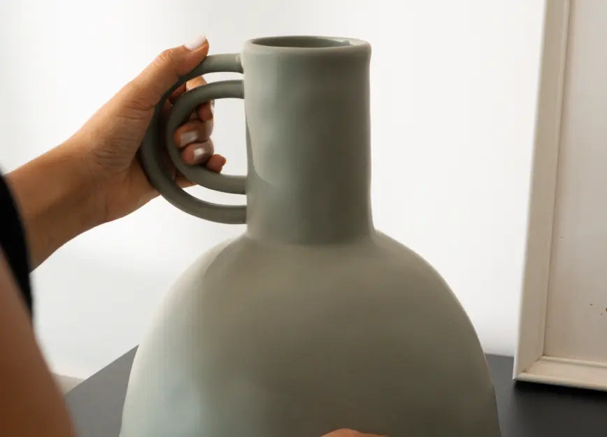 Person holding a large vase with a unique handle design against a plain background