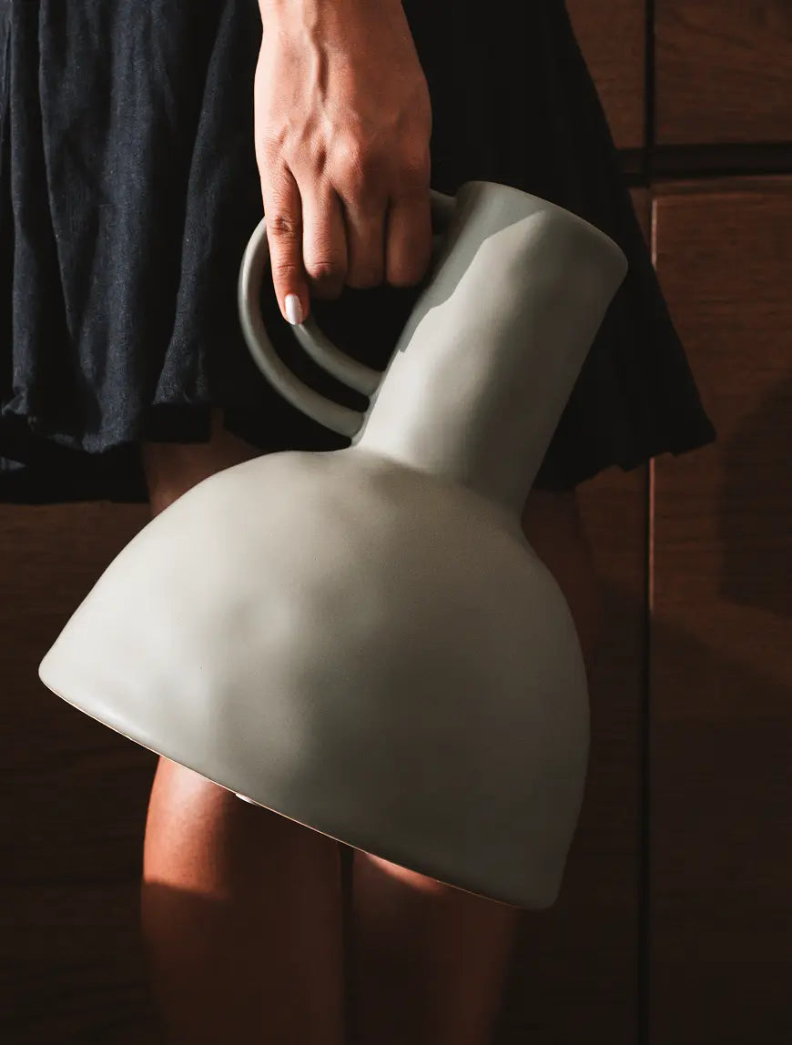 Person holding a large ceramic vase with a dark background