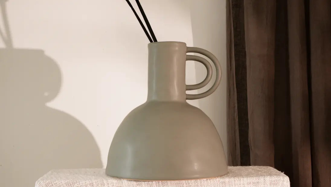 Green ceramic vase on a white surface with a blurred background