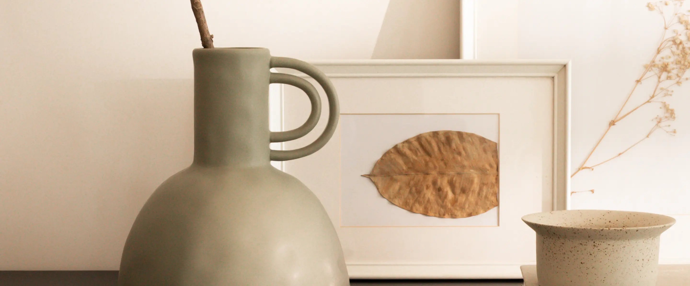 Green ceramic vase with a framed picture of a leaf on a neutral background