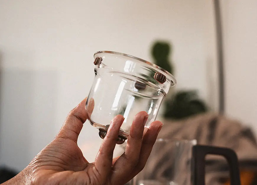 Hand holding the glass tea strainer from the Pourfect Tea Infuser, highlighting its detachable design.